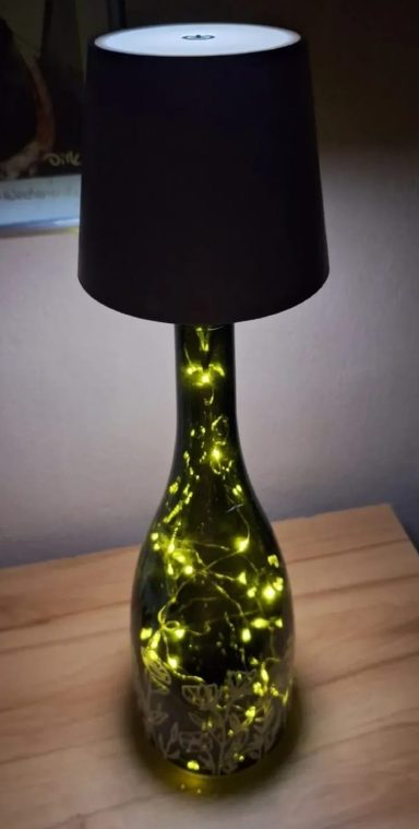 Upcycling Glaslampe mit schwarzem Schirm und leuchtenden, gelben Lichtern im Inneren.