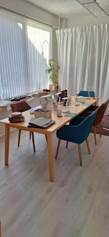 Aufbau Workshopraum Ein gedeckter Esstisch mit Geschirr und Blumen in einem hellen Raum.