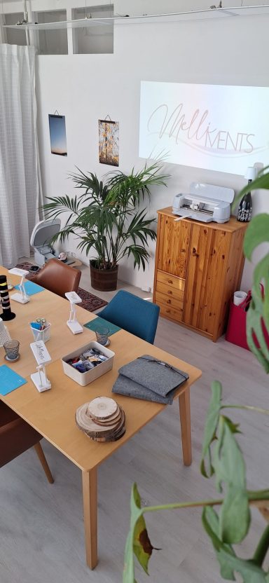 Aufbau Workshopraum Heller Besprechungsraum mit Tisch, Stühlen, Pflanzen und Präsentation auf der Wand.